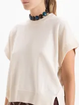 Chaleco de tejido de punto en color celeste, con cuello redondo y mangas cortas con terminación en rib. Presenta un diseño holgado con aberturas laterales en el ruedo y un pequeño bordado decorativo en la parte inferior.