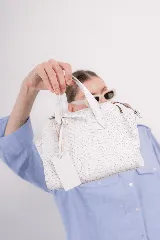 Cartera blanca de cuero con textura geométrica en relieve, doble asa corta y cierre superior con cremallera.