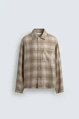 Camisa relaxed fit de manga larga con cuello solapa, confeccionada en tejido con mezcla de viscosa. Presenta un bolsillo plastrón en el pecho, bajo con aberturas laterales y cierre frontal de botonadura. El diseño es a cuadros en tonos beige y marrón.