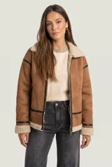 Campera tipo gamulán color camel con interior y cuello de corderito sintético en tono crudo. Presenta cierre frontal, detalles de ribetes en cuero sintético negro y puños con vuelta de corderito.