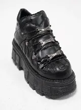Botas de plataforma estilo chunky color negro, confeccionadas en cuero sintético. Presentan un diseño robusto con suela dentada, cordones negros y detalles metálicos decorativos en el empeine.