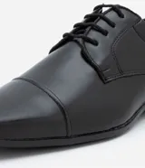 Zapato de vestir negro, confeccionado en cuero sintético, con puntera cuadrada, cierre con cordones y suela de goma.