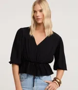 Blusa negra de viscosa con escote en V cruzado, mangas cortas con elástico en los puños y peplum ajustado en la cintura con lazo regulable.