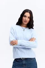 Buzo de punto color celeste con diseño de trenzas en relieve, cuello redondo y mangas largas con puños acanalados.