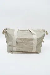 Bolso de viaje tipo duffel color beige, con asas de mano de cinta resistente, bolsillo frontal con cierre y cierre inferior ampliable.