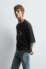 Camiseta de punto de algodón, corte boxy fit, color negro con efecto lavado. Presenta un estampado gráfico frontal que simula un ojo o forma ovalada con texto ilegible en su interior.