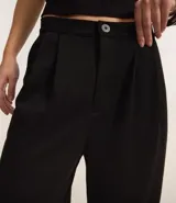 Pantalón wide leg negro confeccionado en algodón, con pliegues delanteros y cierre por botón y cremallera.