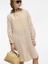 Vestido túnica camisera color negro con botones en la parte delantera, cuello mao y detalle de bordado en el pecho y mangas. Presenta tajos verticales laterales.