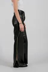 Pantalón de cuero negro, tiro alto, con corte recto y ancho. Presenta un detalle de bordado artesanal en los laterales exteriores de las piernas.