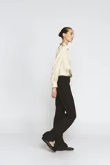 Camisa de cuello solapa y manga larga con puños anchos, confeccionada en tejido satinado color beige. Presenta cierre frontal con botones ocultos y bajo ajustable mediante cordones del mismo tejido.