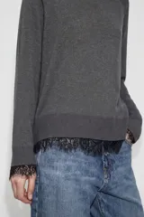 Jersey de cuello redondo y manga larga, confeccionado en tejido de punto fino. Presenta un diseño liso con aplicación de encaje negro en el bajo y en los puños.