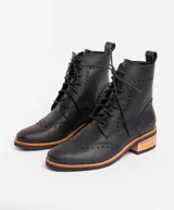 Botas acordonadas estilo borcego, confeccionadas en cuero vacuno negro. Presentan detalles de perforaciones decorativas tipo brogue en la puntera y laterales, con suela y taco de madera en tono natural.