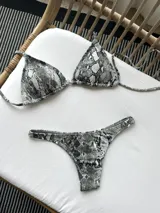 Conjunto de bikini con estampado de piel de serpiente en tonos grises. El top es de triángulos movibles con almohadillas desmontables y se ata al cuello y a la espalda. La bombacha es colaless con laterales fijos.