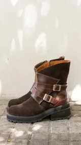 Botas de caña media combinadas en gamuza y cuero vacuno color marrón oscuro. Presentan un diseño con tiras decorativas cruzadas sobre el empeine con hebillas metálicas, cierre lateral y suela de goma con plataforma dentada.