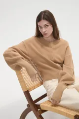 Saco de punto color beige, con cuello redondo, cierre frontal con botones y mangas largas con puños acanalados.