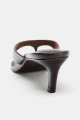 Sandalia tipo mule de piel color marrón oscuro, con diseño de tira entre los dedos y tacón fino de altura media.