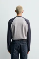Camiseta de corte relajado con diseño color block, cuerpo en gris melange y mangas largas raglán en color azul marino. Presenta cuello redondo al tono de las mangas y bajo con acabado irregular.
