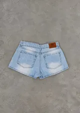 Short de jean tiro bajo color celeste con efecto desgastado, bolsillos traseros y etiqueta de cuero marrón en la cintura.