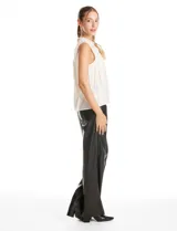 Blusa sin mangas color blanco, confeccionada en crepe con acabado satinado. Presenta un cuello alto decorado con mostacillas y una sobrecapa drapeada en el frente. La espalda cuenta con una abertura tipo gota y cierre de botón.