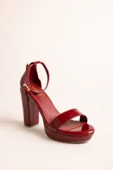 Sandalias de tacón alto con plataforma, confeccionadas en cuero con acabado brillante tipo charol, color negro. Poseen tira delantera ancha, tira ajustable al tobillo con hebilla metálica dorada, y taco ancho.