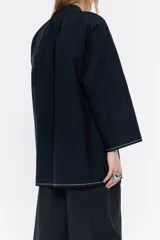 Camisa blanca de algodón, de corte línea A, con cuello mao con lazo a modo de cierre y manga larga ancha con pespunte bordado en puños.