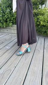 Sandalia de tacón cuadrado medio, con diseño de tiras horizontales y punta cuadrada. Presenta un acabado metalizado en color turquesa y cierre con pulsera al tobillo.