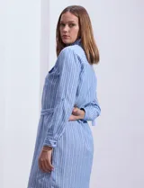Vestido camisero corto a rayas verticales celestes y blancas, con cuello con solapa, abertura frontal con botones, dos bolsillos de parche en el pecho y lazo de ajuste en la cintura.