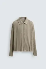 Chaqueta de punto con textura de trenzas verticales, color beige, cuello solapa y cierre frontal con cremallera.