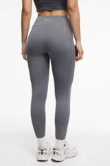 Calza deportiva larga color gris, con cintura alta, detalles de transparencias laterales en tul y bolsillos laterales.