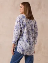 Blusa estampada con flores azules sobre fondo blanco, marca Floral & Ivy. Tiene cuello a la base con escote en V y aplique de botones. Las mangas son tres cuartos con puño y botón. Presenta tajos en las costuras laterales.