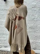 Ruana abierta de lana merino en color beige, con diseño de corte amplio y terminaciones con flecos en el ruedo.