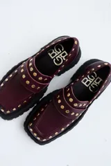 Mocasines de cuero color marrón con suela track negra y tachas doradas.