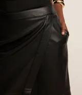 Falda midi negra de cuero sintético con diseño cruzado tipo sobre, bolsillos laterales y cierre trasero.