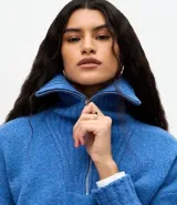 Suéter de punto azul con cuello alto y cierre frontal de cremallera metálica. Presenta textura de líneas verticales, corte regular, mangas largas y terminaciones acanaladas.