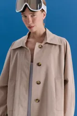 Trench midi de color camel, confeccionado en una mezcla de algodón y nylon con propiedades repelentes al agua. Presenta un diseño clásico con cuello camisero, cierre frontal de botones, bolsillos laterales y tajos en los costados.