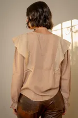Blusa blanca de algodón con cuello redondo, mangas largas con puños elásticos y volados decorativos en los hombros.