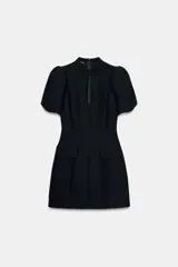 Vestido corto negro con cuello redondo y escote pico frontal, manga corta abullonada y cintura entallada. Presenta tapetas decorativas en la parte inferior delantera.