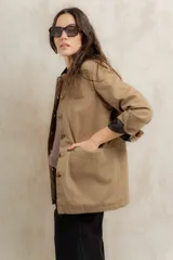 Campera color beige con cuello de corderito negro, cierre frontal con botones y forro interior. Presenta un diseño de corte recto y mangas largas con puños vueltos.