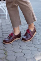 Zapato náutico de cuero color marrón con cordones rojos y suela color caramelo.