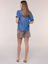 Camisa de lyocell color azul con efecto denim, cuello camisero, cierre frontal con botones y detalles de bordado oscuro a lo largo de la botonera. Presenta mangas cortas abullonadas con puños elásticos y terminación con volados.