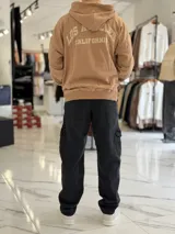 Canguro oversize beige con capucha y cordones ajustables, bolsillo tipo canguro y pequeño bordado en el pecho.