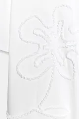 Camiseta blanca de algodón con cuello redondo, manga corta y detalle de flor en relieve bordada en el mismo tono.
