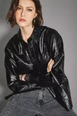 Campera negra de cuero sintético con acabado brillante, cuello camisero, cierre frontal con botones y dos bolsillos delanteros con solapa.