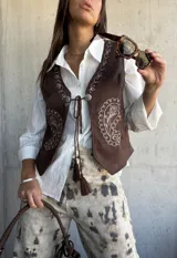 Chaleco de gamuza color chocolate con bordados decorativos en color crudo y cierre frontal con cordones y borlas.