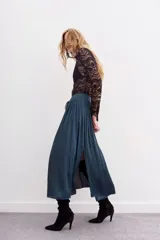 Falda larga negra de poliéster con cintura elastizada tipo nido de abeja, tiras de ajuste con terminales metálicas y detalle de hilo de lurex, y tajo lateral.