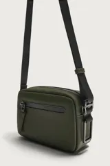 Bandolera porta teléfono de acabado engomado en color verde militar. Cuenta con un compartimento principal y un bolsillo frontal con cierre de cremallera, además de un bolsillo interior también con cierre. Incluye asa de hombro ajustable y extraíble, y detalle de mosquetón en el lateral.