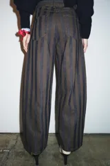 Jeans de tiro medio con corte barrel leg, confeccionados en denim con rayas verticales a contraste en tonos azul oscuro y marrón/tostado. Presentan cinco bolsillos y cierre frontal con cremallera y botón.
