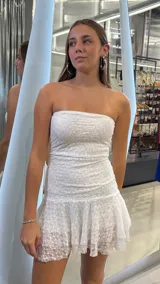 Vestido corto de encaje blanco, con diseño strapless y falda con volado en el ruedo.