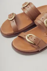 Sandalias planas de cuero negro con diseño de dos tiras ajustables con hebillas metálicas.