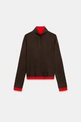 Jersey de punto con efecto doble, cuello subido y manga larga. Presenta un diseño en color marrón con detalles en rojo vibrante en el cuello, puños y ruedo. Cuenta con cierre frontal parcial mediante botones.